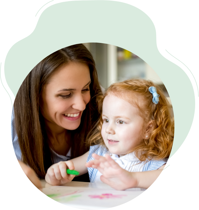 A photograph of a woman watching a young girl draw with crayons.